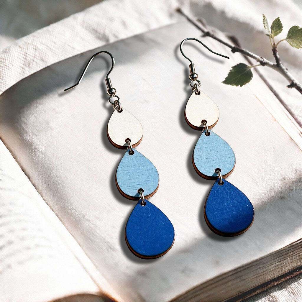 Blue Raindrops plywood earrings made in Finland, photographed on a vintage book in natural sunlight