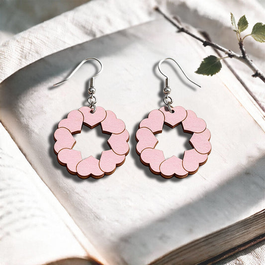 Light pink Kiss plywood earrings made in Finland, photographed on a vintage book in natural sunlight