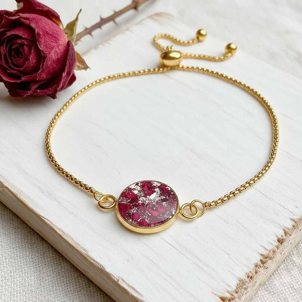 Rose Petal Bracelet with real preserved rose petals in resin, set in a gold-plated stainless steel adjustable sliding chain bracelet, displayed on a white wooden board with a dried rose.