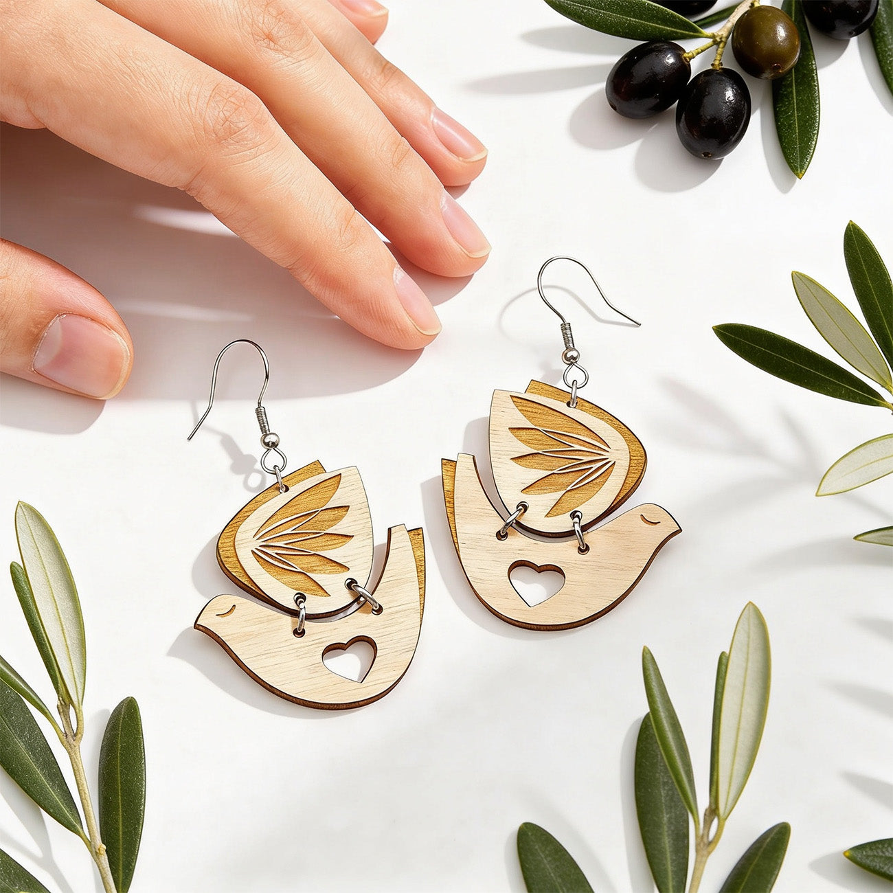 Peace Dove wooden earrings by byMinta photographed with olive branches and a hand for scale in soft natural daylight.