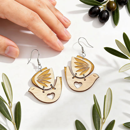Peace Dove wooden earrings by byMinta photographed with olive branches and a hand for scale in soft natural daylight.