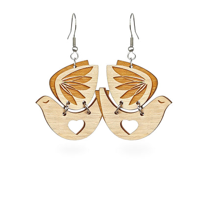Wooden bird earrings by byMinta with laser-cut leaf details and heart accents, photographed in a soft Nordic forest setting.