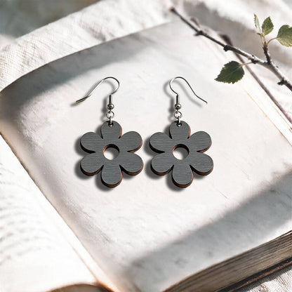 Grey Retro Flower plywood earrings made in Finland, photographed on a vintage book in natural sunlight