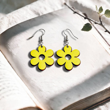 Yellow Retro Flower plywood earrings made in Finland, photographed on a vintage book in natural sunlight