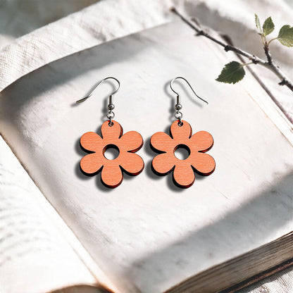 Coral Retro Flower plywood earrings made in Finland, photographed on a vintage book in natural sunlight