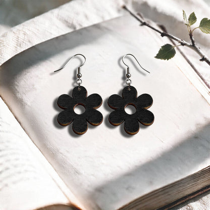 Black Retro Flower plywood earrings made in Finland, photographed on a vintage book in natural sunlight