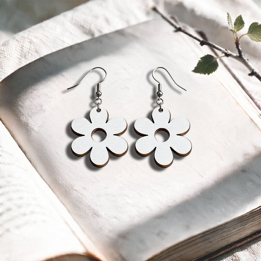 White Retro Flower plywood earrings made in Finland, photographed on a vintage book in natural sunlight