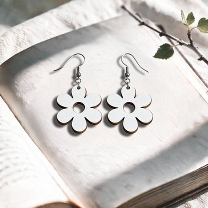 White Retro Flower plywood earrings made in Finland, photographed on a vintage book in natural sunlight