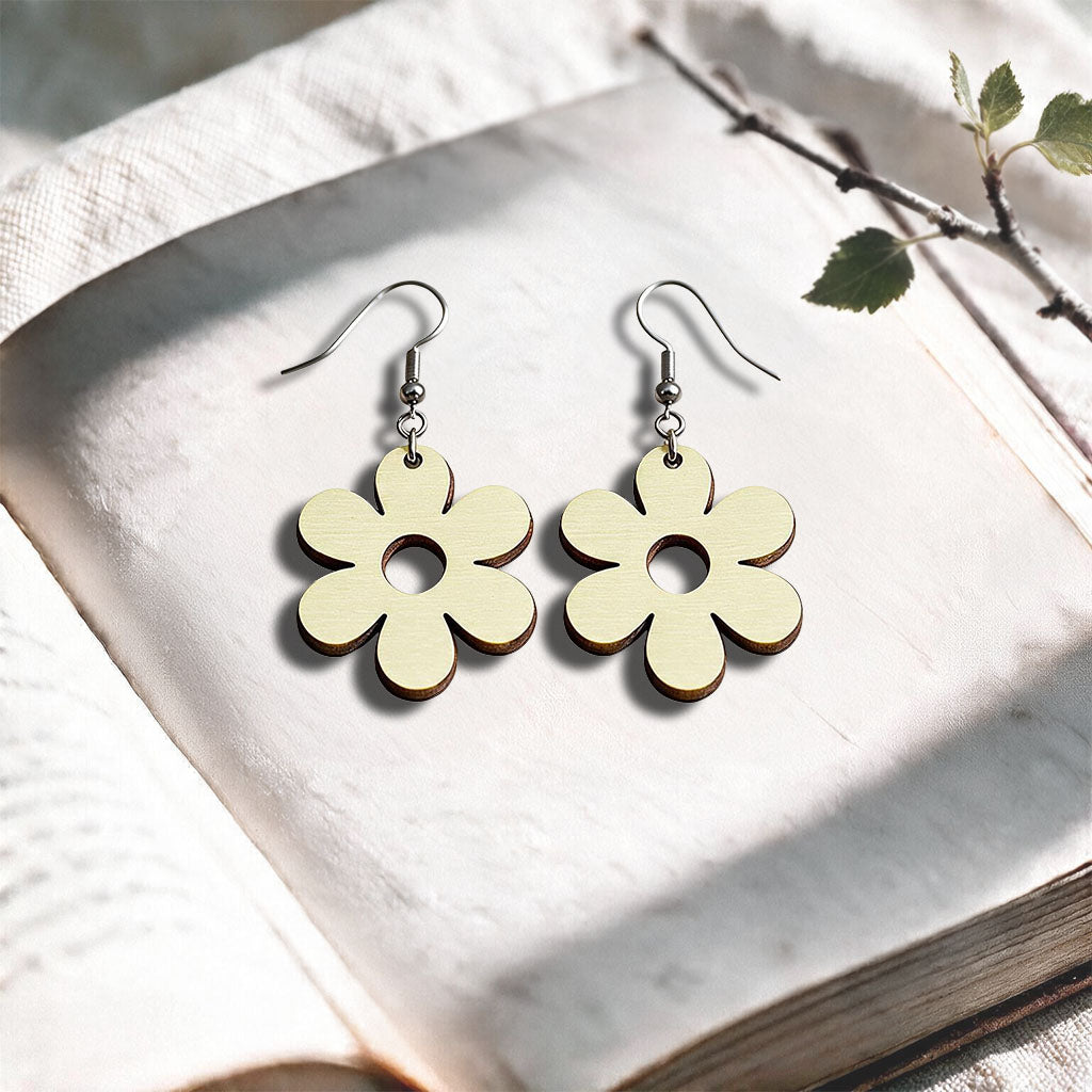 Vanilla Retro Flower plywood earrings made in Finland, photographed on a vintage book in natural sunlight