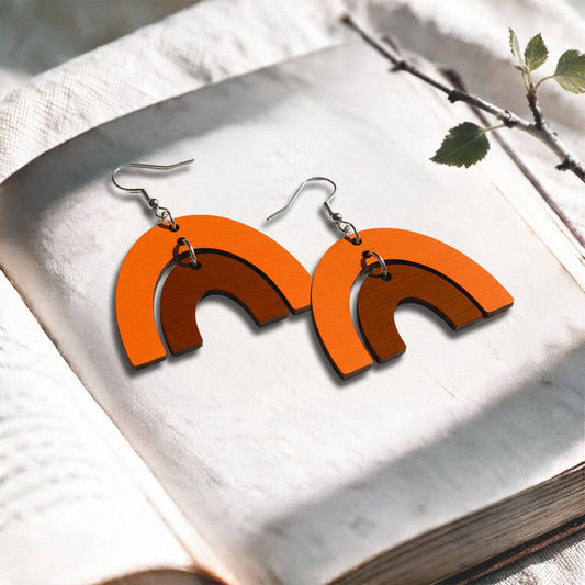 Orange and brown Riemukaari plywood earrings made in Finland, photographed on a vintage book in natural sunlight