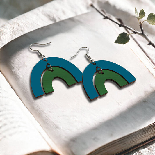 Bluepetrol and green Riemukaari plywood earrings made in Finland, photographed on a vintage book in natural sunlight