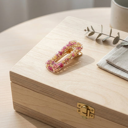 Floral resin hair clip with rose petals on wooden box in soft daylight
