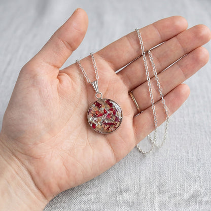Handmade resin necklace with real rose petal fragments and silver leaf flakes shown in an open hand for size reference.