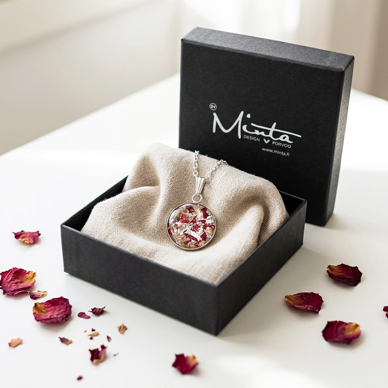 Handmade resin necklace with real rose petal fragments and silver leaf flakes presented in a gift box with linen fabric and rose petals.