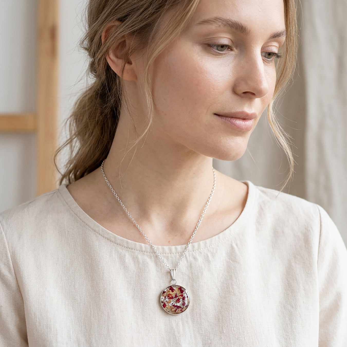 Woman wearing a handmade resin necklace with real rose petal fragments and silver leaf flakes, round floral pendant on a stainless steel chain.