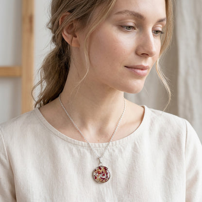 Woman wearing a handmade resin necklace with real rose petal fragments and silver leaf flakes, round floral pendant on a stainless steel chain.
