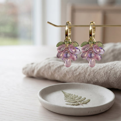 Plum Cluster Earrings with translucent purple glass beads, detachable charm and gold-plated huggie hoops on a soft linen background. Handcrafted in Finland.