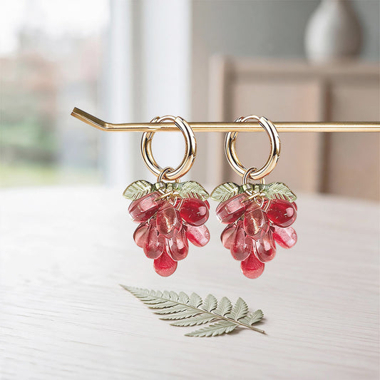 Red Currant Cluster Earrings with translucent red glass beads, detachable charm and gold-plated huggie hoops on a soft linen background. Handcrafted in Finland.