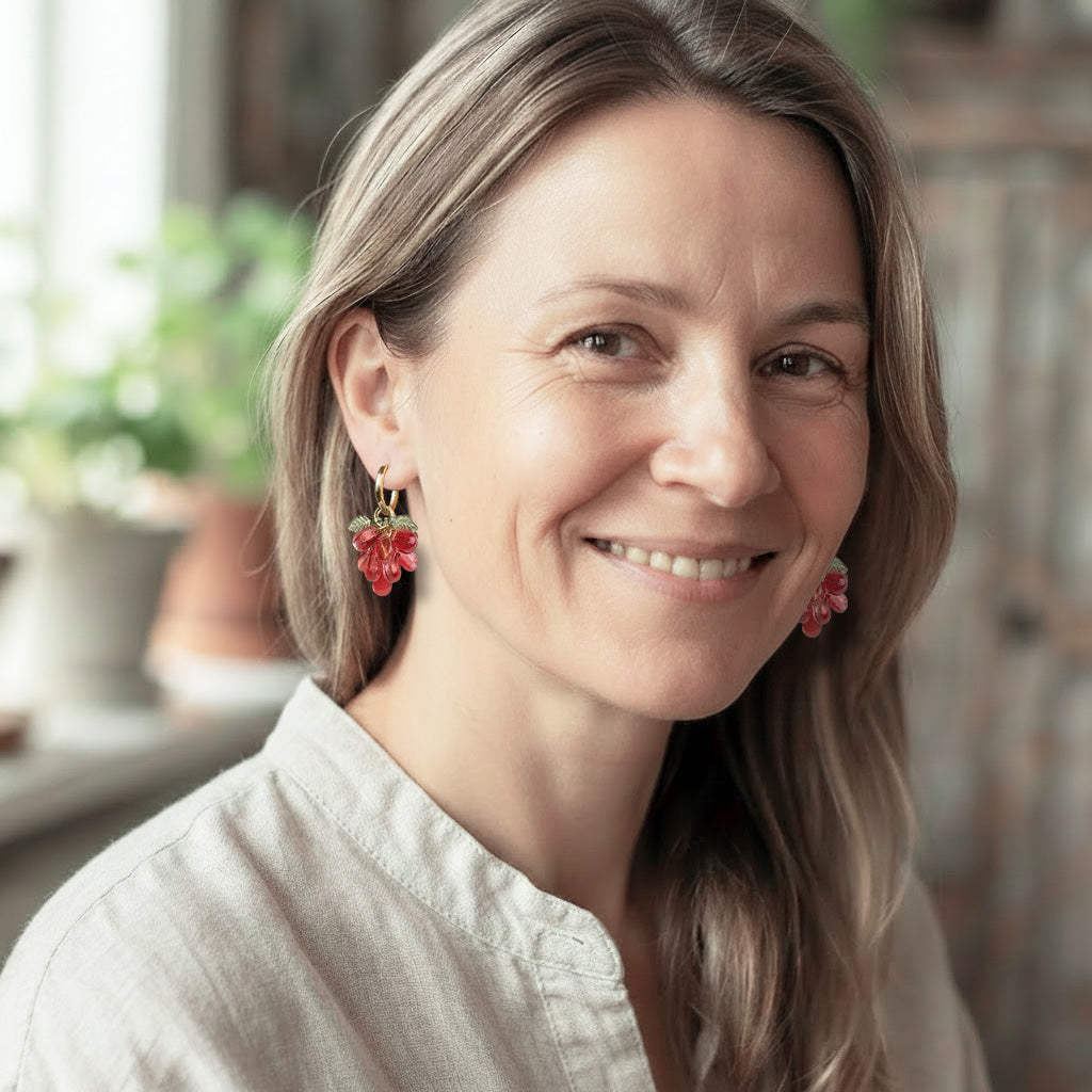 Woman wearing Red Currant Cluster Earrings with translucent red glass beads and gold-plated huggie hoops. Handcrafted in Finland.