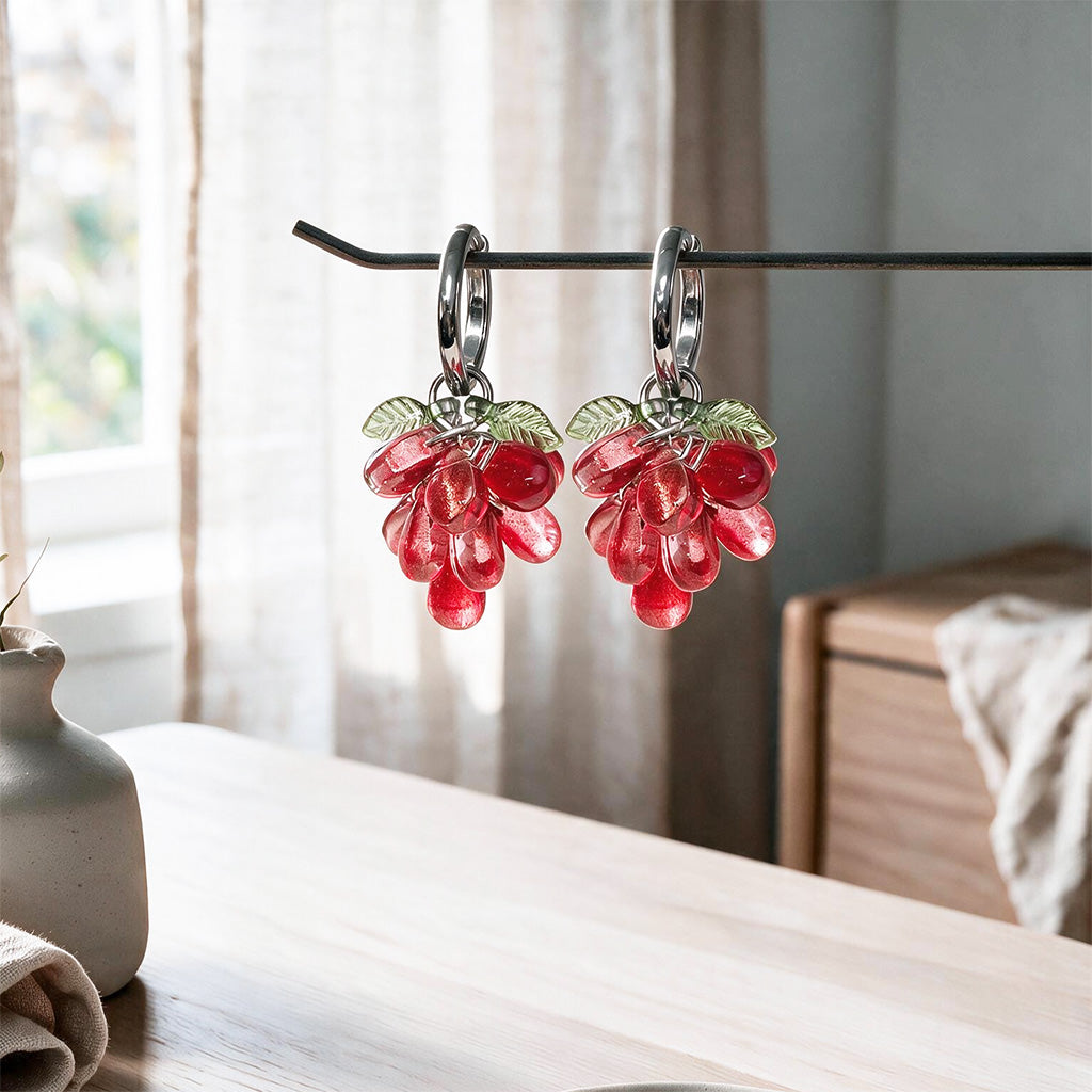 Red Currant Cluster Earrings hanging on a display stand with translucent red glass beads and gold-plated huggie hoops. Handcrafted in Finland.