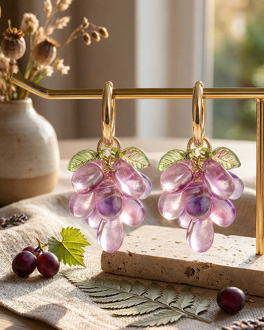 Violet Crush Grape glass bead earrings with gold-tone hoops, displayed on a gold jewelry stand in warm natural sunlight.