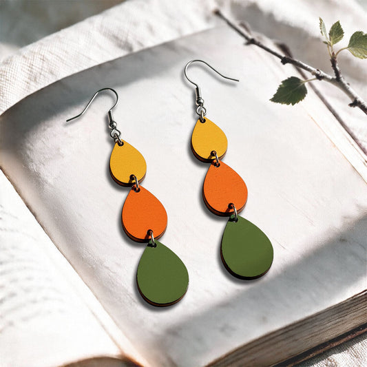 Green, orange and lion Sadetta plywood earrings made in Finland, photographed on a vintage book in natural sunlight