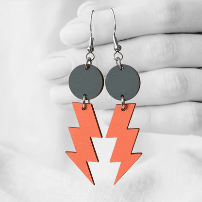 Orange and dark grey Salamat (lightning bolt) plywood earrings made in Finland, photographed against a black and white background of a hand.