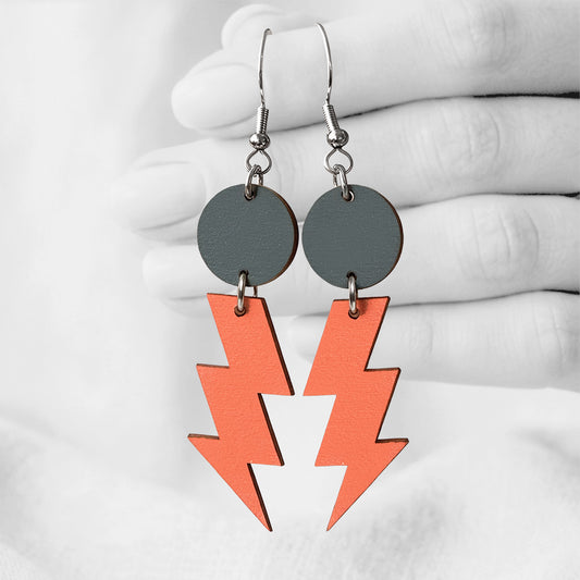 Orange and dark grey Salamat (lightning bolt) plywood earrings made in Finland, photographed against a black and white background of a hand.