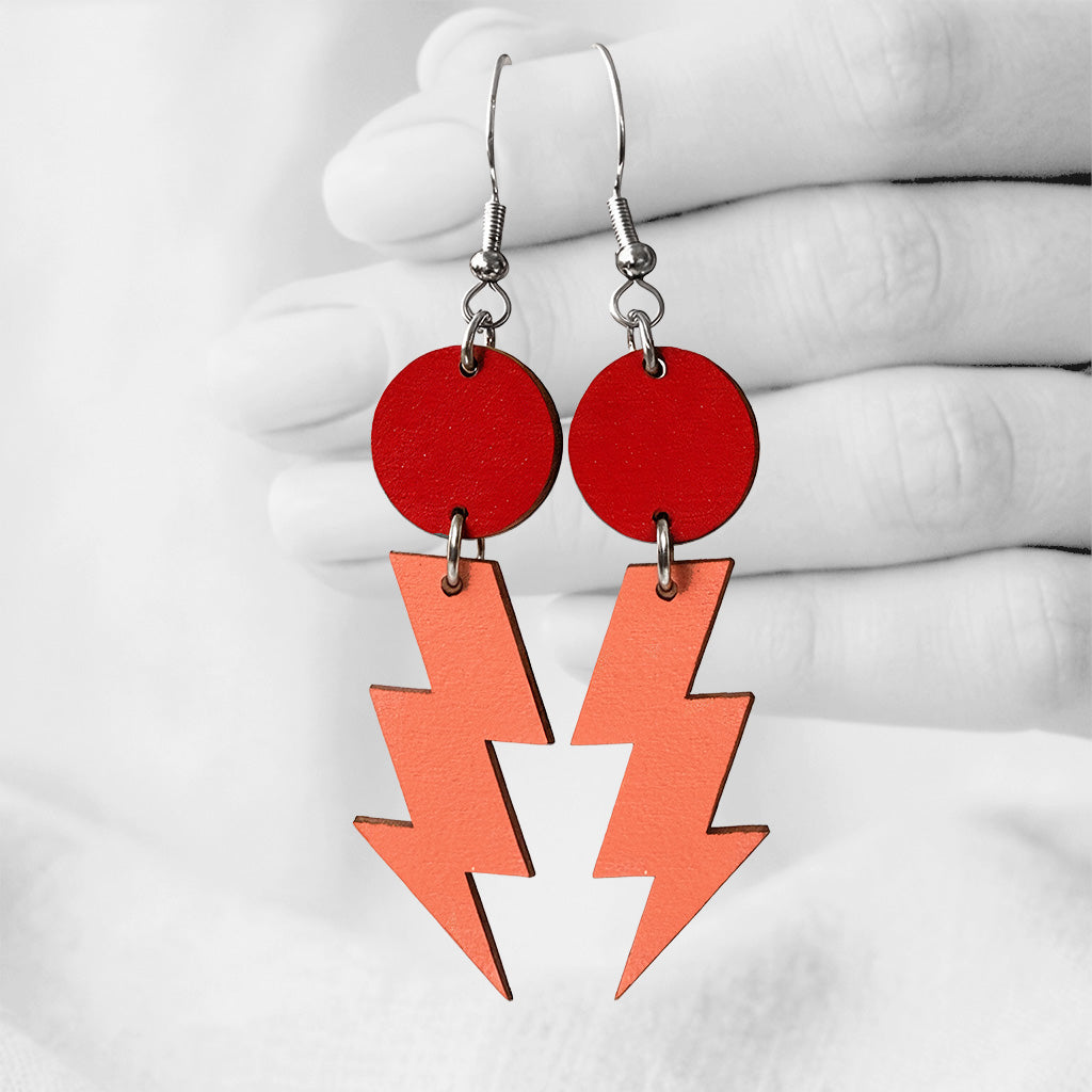 Red and orange Salamat (lightning bolt) plywood earrings made in Finland, photographed against a black and white background of a hand.