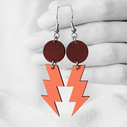 walnut and orange Salamat (lightning bolt) plywood earrings made in Finland, photographed against a black and white background of a hand.