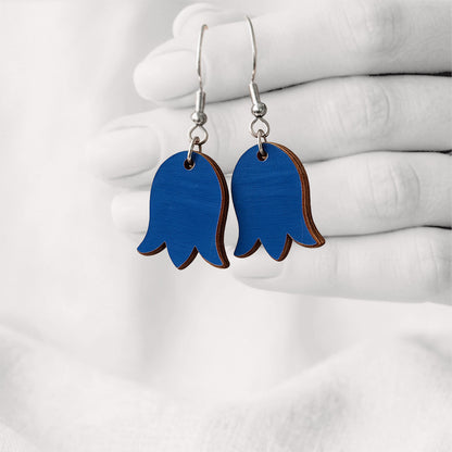Blue bellflower-shaped plywood earrings handmade in Finland, hanging from a hand against a softly blurred light linen background.