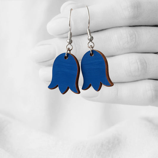 Blue bellflower-shaped plywood earrings handmade in Finland, hanging from a hand against a softly blurred light linen background.
