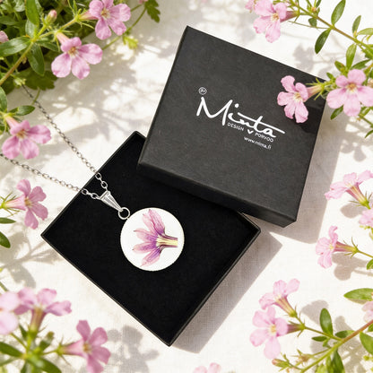 Handmade resin necklace with a real pink fan flower (Scaevola) displayed in a black jewelry box surrounded by delicate pink fan flowers. Botanical jewelry photographed in bright natural daylight with a soft and airy summer atmosphere.