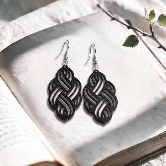 Black Solmu plywood earrings made in Finland, photographed on a vintage book in natural sunlight