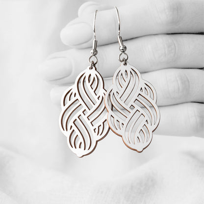 White Solmu (Knot) plywood earrings handmade in Finland, photographed hanging against a black-and-white hand background.