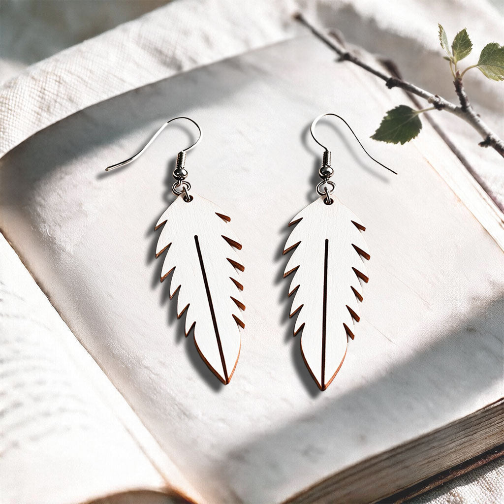 White Feather plywood earrings made in Finland, photographed on a vintage book in natural sunlight