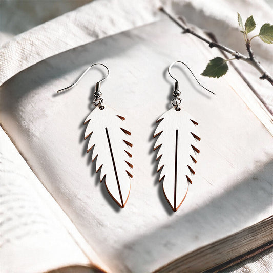 White Feather plywood earrings made in Finland, photographed on a vintage book in natural sunlight