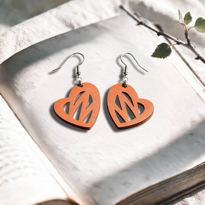 Coral Heartbeat plywood earrings made in Finland, photographed on a vintage book in natural sunlight