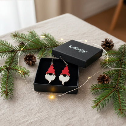 Christmas gnome earrings presented in a gift box with spruce branches, pinecones, and warm fairy lights, creating a cozy holiday atmosphere. Handmade in Finland by byMinta.