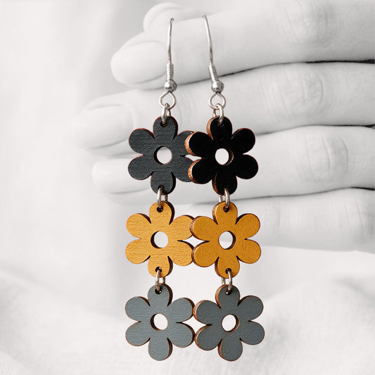 Black, yellow and grey TriplaRetro plywood earrings handmade in Finland, shown hanging from a hand against a light linen background