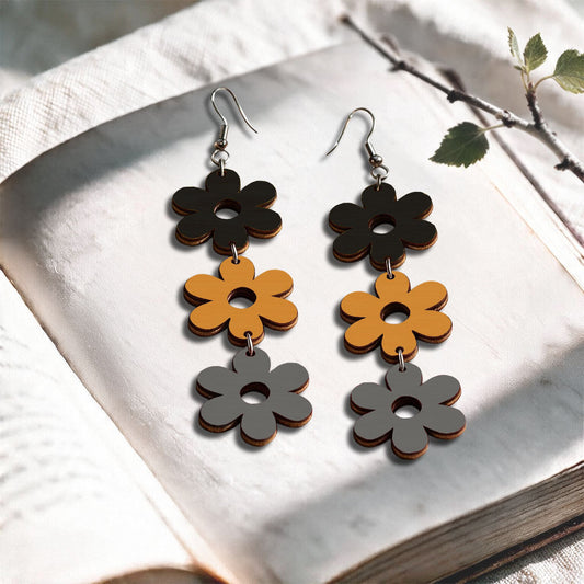 Gray, lion and black flower plywood earrings made in Finland, photographed on a vintage book in natural sunlight