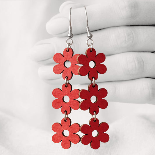 Red TriplaRetro plywood earrings handmade in Finland, shown hanging from a hand against a light linen background