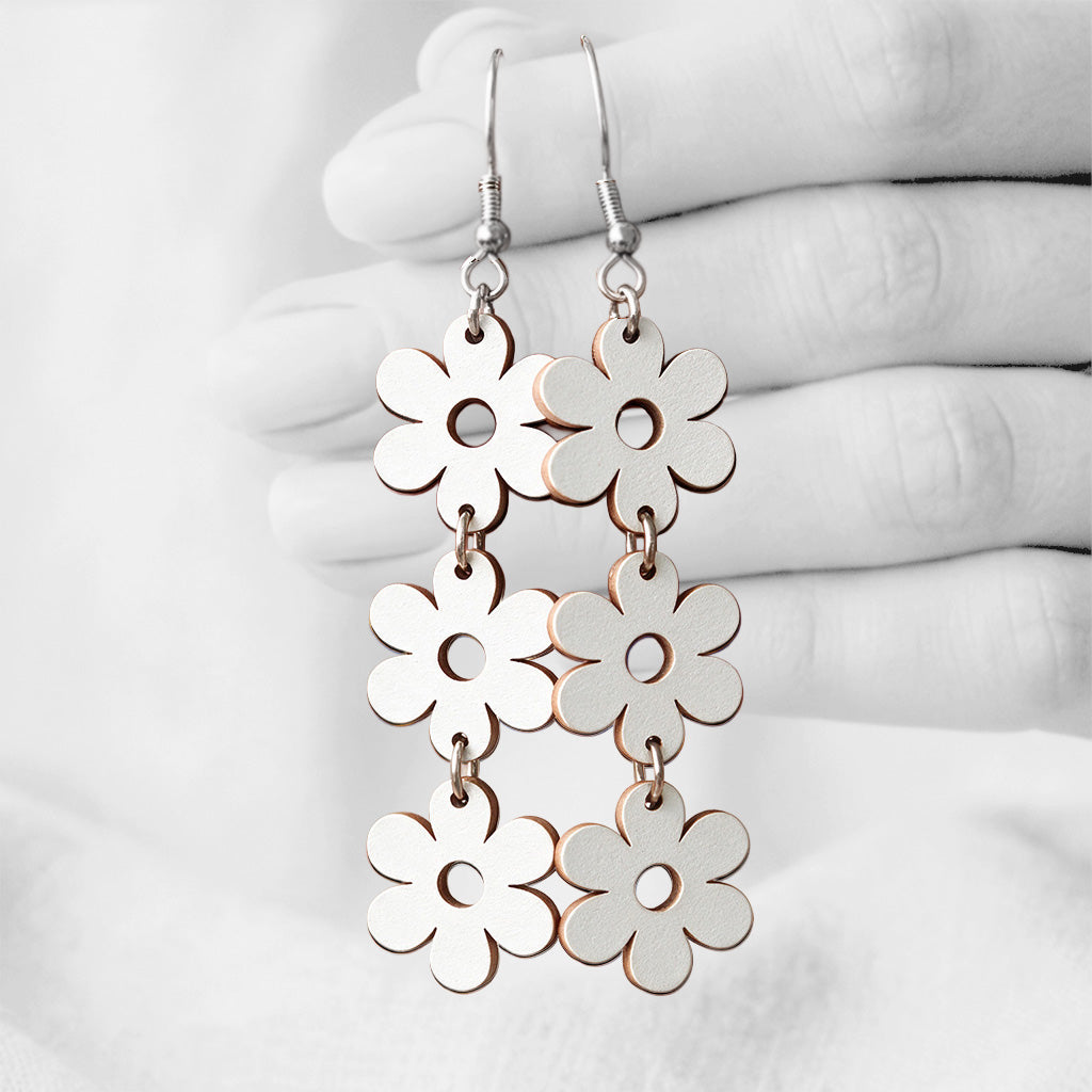 White TriplaRetro plywood earrings handmade in Finland, shown hanging from a hand against a light linen background