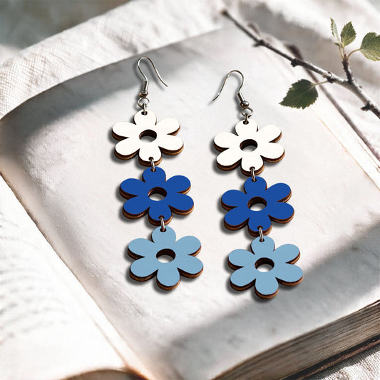 White, blue and light blue flower plywood earrings made in Finland, photographed on a vintage book in natural sunlight