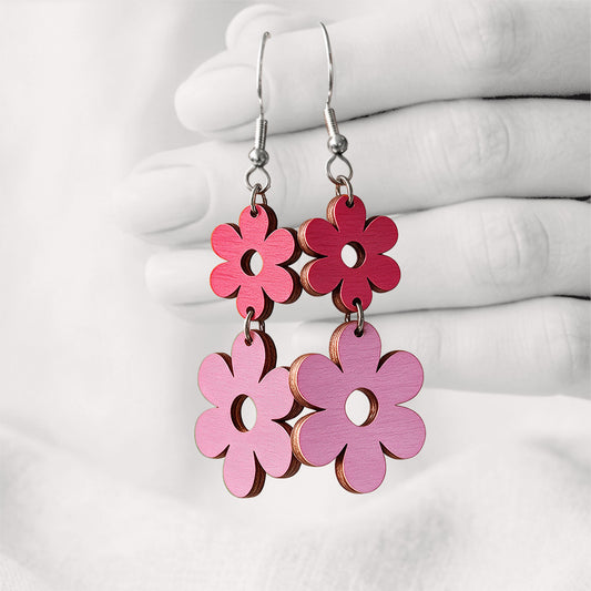 Raspberry and mauve TuplaRetro Duo plywood earrings made in Finland, photographed hanging from a hand against a softly blurred light linen background.
