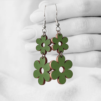 Moss Green Double Retro plywood earrings made in Finland, photographed hanging from a hand in black and white against a softly blurred light background.