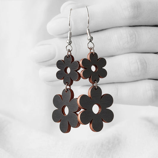 Black Double Retro plywood earrings made in Finland, photographed hanging from a hand in black and white against a softly blurred light background.