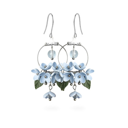 Mist Flower Hoop Earrings featuring delicate pale blue flowers, green leaves, and sparkling crystal details. Handmade in Finland by byMinta.