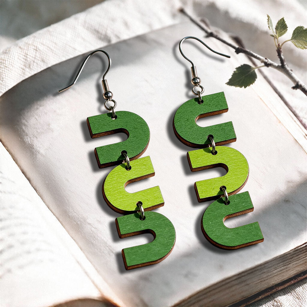 Green and lime U-Turn plywood earrings made in Finland, photographed on a vintage book in natural sunlight