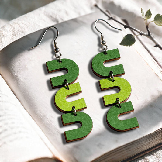 Green and lime U-Turn plywood earrings made in Finland, photographed on a vintage book in natural sunlight